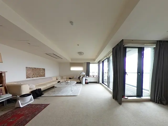 Spacious living room with an L-shaped beige sofa, white coffee table on a light rug, and floor-to-ceiling glass doors leading to a balcony.