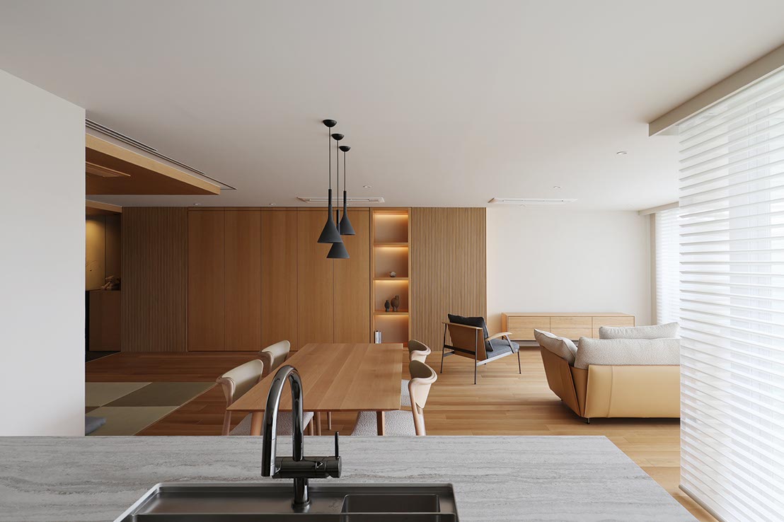 Open-concept living and dining area with a marble kitchen island, black faucet, wooden dining table, and a tan sofa by large windows.
