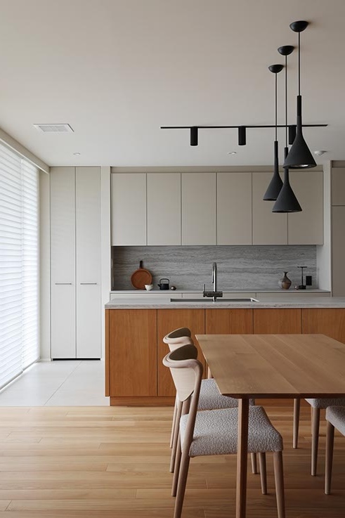 Modern kitchen with a wooden island, gray cabinets, and a dining table with upholstered chairs under black pendant lights.