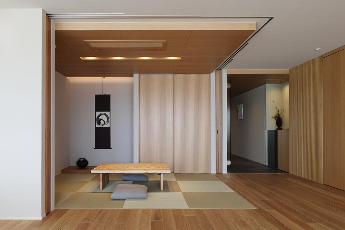 Minimal Japanese-style seating area with a low wooden table on tatami mats and soft cushions, framed by sliding doors and warm lighting.