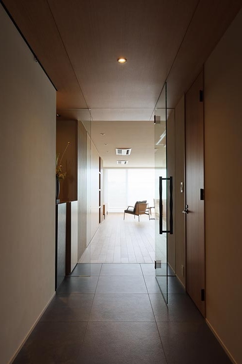 Long, well-lit office hallway with glass doors opening to a bright seating area at the end.