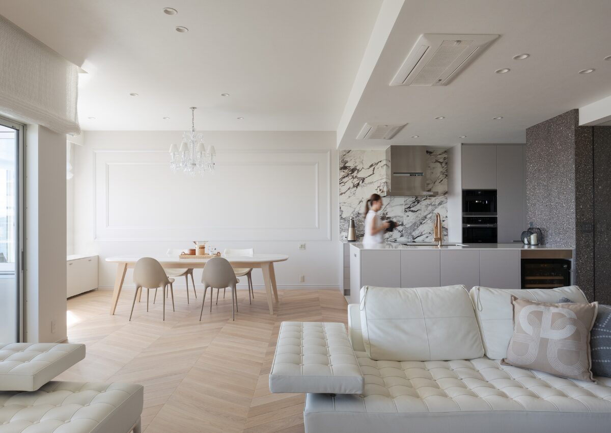Open-concept living/dining area in white: tufted sofa, marble kitchen backsplash, and light wood floors.