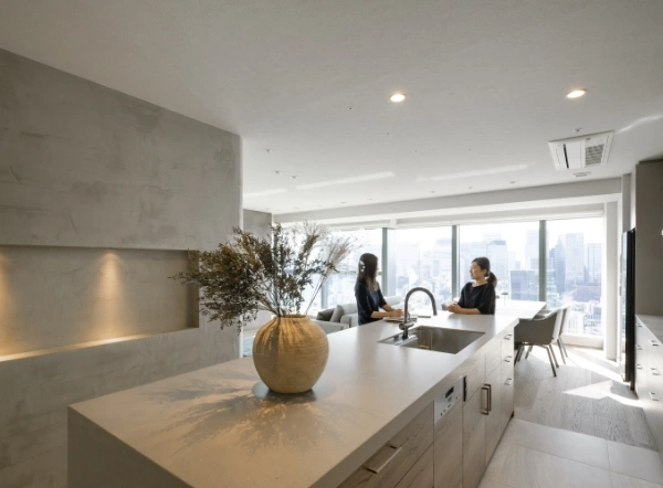 Two people chat in a bright, modern kitchen with a large vase on an island and a city skyline through expansive windows.