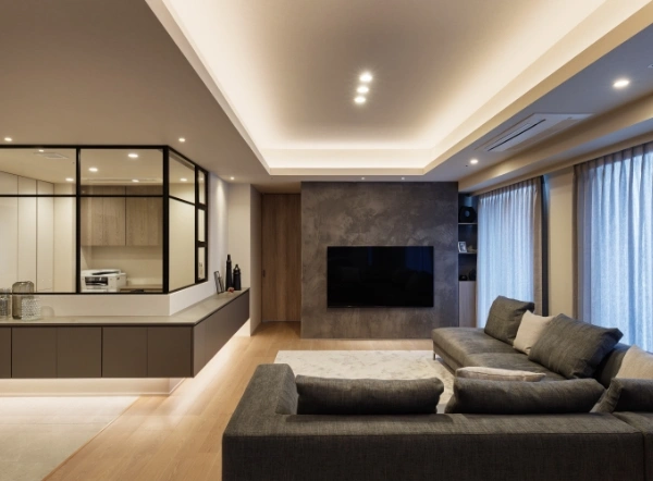 Open-concept living room with a wall-mounted TV, gray sectional sofa, and a glass-partitioned modern kitchen on the left.