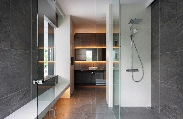 Modern bathroom with a glass-enclosed walk-in shower, grey tiled walls, and a backlit vanity area in the back.