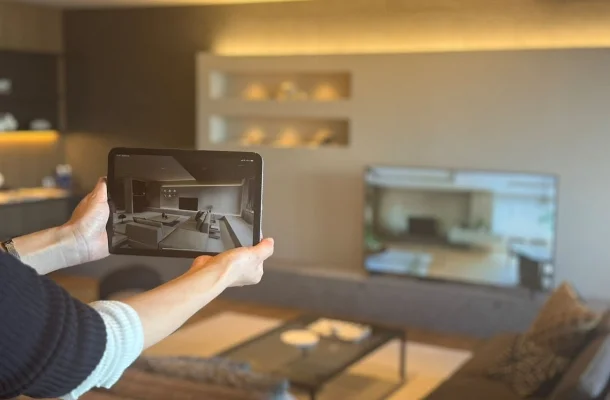 Person holds a tablet showing a modern living room layout while the same room is displayed on a TV in the background.