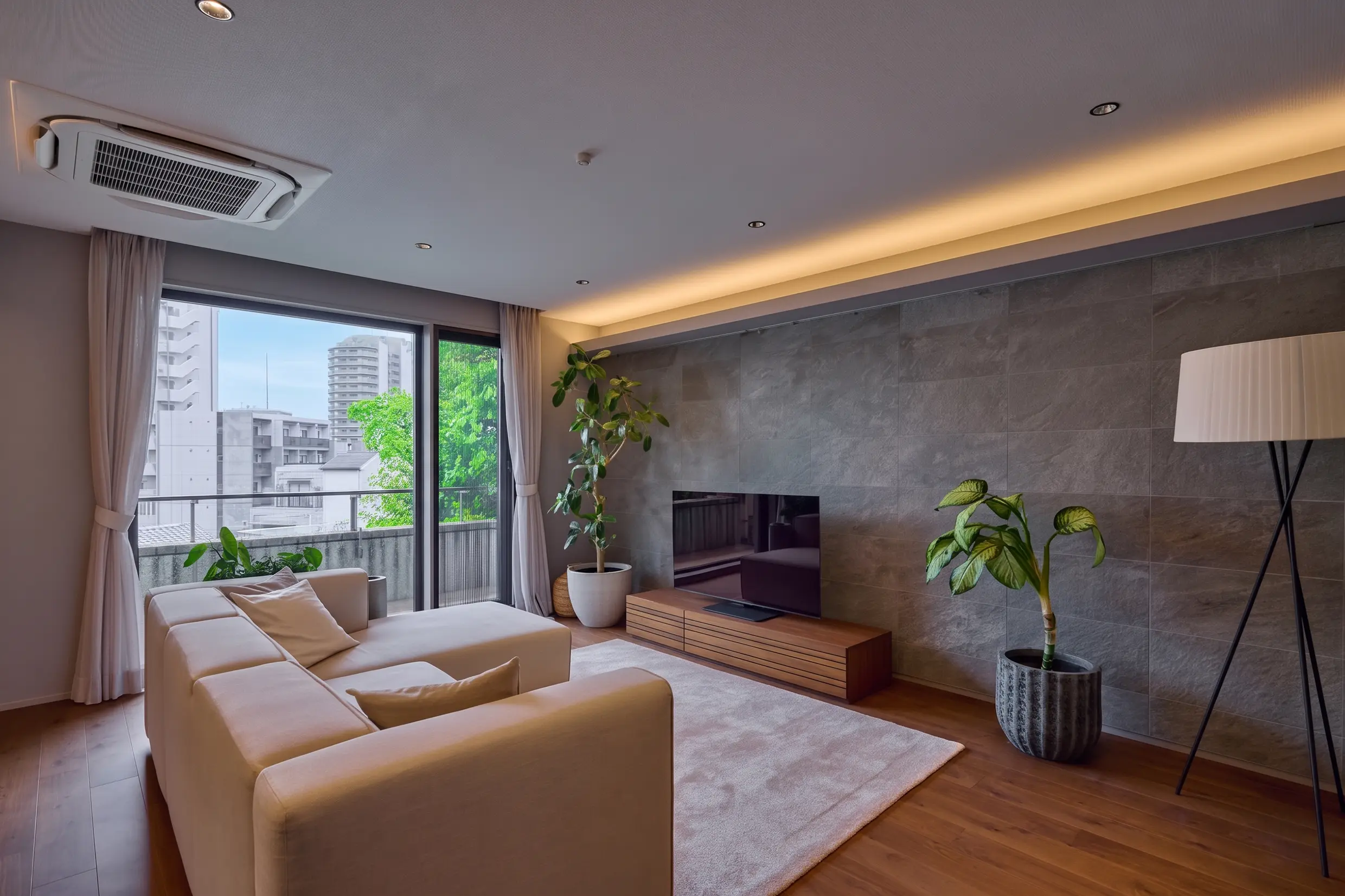 Bright contemporary living room with a white sectional sofa, large windows, and potted plants by a stone accent wall. (Informative)