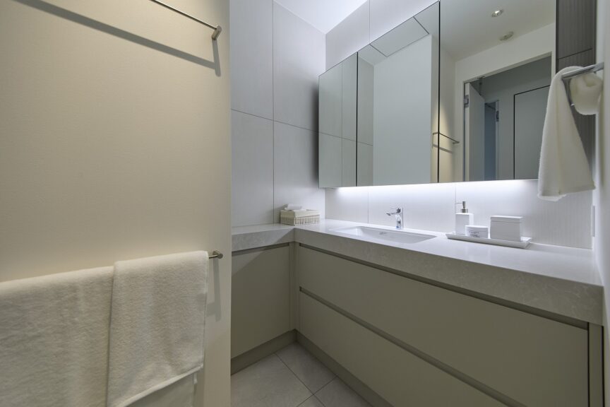 Modern bathroom vanity with large backlit mirror, white countertop, and gray cabinetry around a rectangular sink