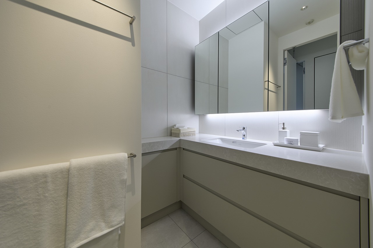 Modern bathroom vanity with large backlit mirror, white countertop, and gray cabinetry around a rectangular sink