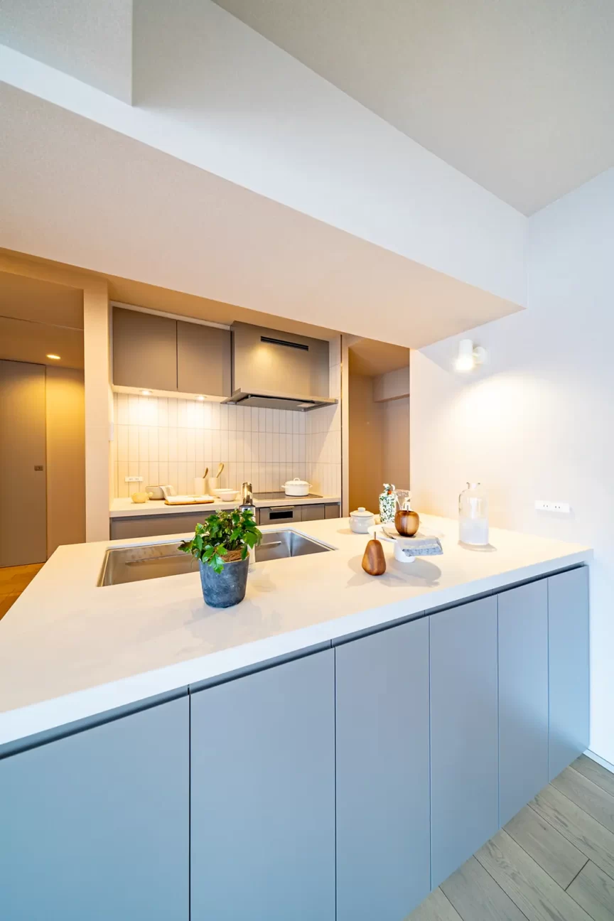 Modern kitchen with a large white island, sink, and gray cabinets, plus stainless steel appliances in the background.