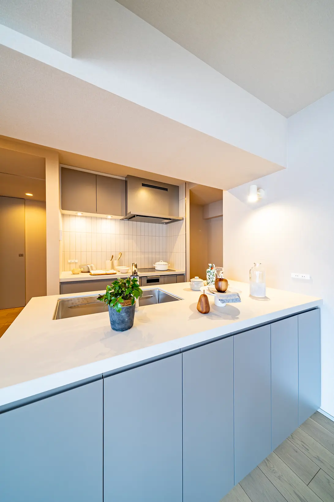 Modern kitchen with a large white island, sink, and gray cabinets, plus stainless steel appliances in the background.
