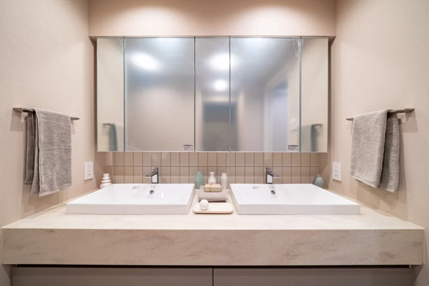 Double-sink bathroom vanity with a wide mirrored medicine cabinet, beige walls, and towels on both sides.